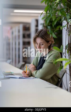 Academic career. Female university professor taking notes in day planner while sitting in library Stock Photo