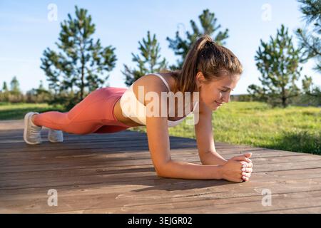 Fit young athletic woman doing planking exercise working on abdominal muscles and triceps outdoors. Stock Photo