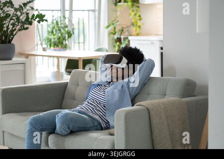 Impressions smiling African American young woman using VR headset immersing herself in metaverse Stock Photo