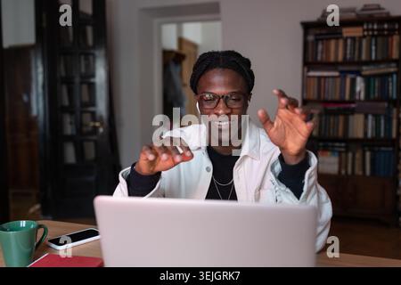 Smiling young African man tutor wearing wireless earbuds talking by webcam teaching online from home Stock Photo