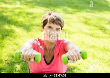 Cheerful senior lady exercising with dumbbells in the park Stock Photo