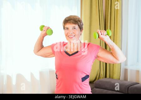 Cheerful senior lady exercising with dumbbells in the home Stock Photo