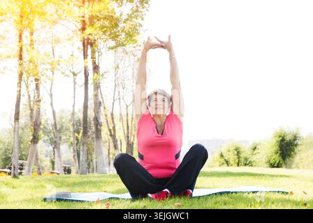 Senior woman doing yoga exercise and stretching on green grass  in the park Stock Photo