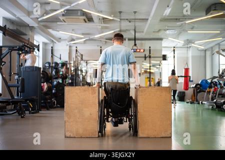 Persistent disabled man in wheelchair with strong stamina doing push ups on cubes with determination Stock Photo