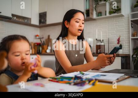 Japanese mother with daughter working from home multitasking Stock Photo
