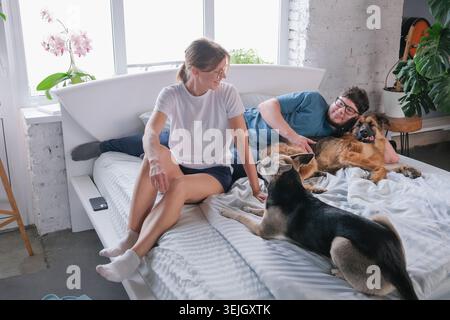 Happy millennial couple having breakfast in bed and enjoying fun time with their dogs Stock Photo