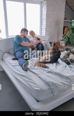Happy millennial couple having breakfast in bed and enjoying fun time with their dogs Stock Photo
