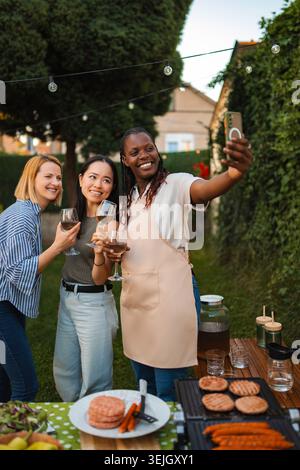 Diverse adult friends taking selfie enjoying outdoor BBQ garden party Stock Photo