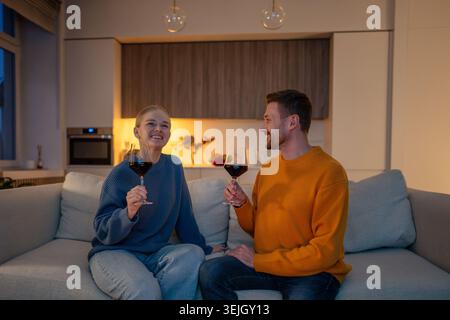 Smiling happy couple toasting with wine glasses, relaxing on sofa in romantic evening at home Stock Photo