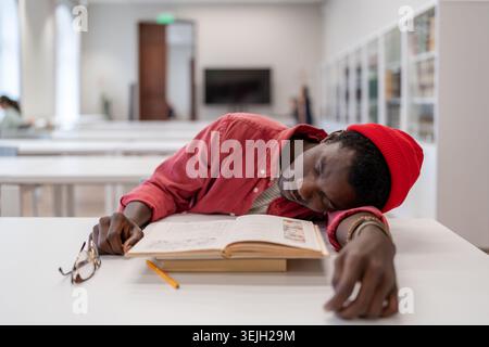 Tired exhausted African guy student falling asleep while studying in library Stock Photo