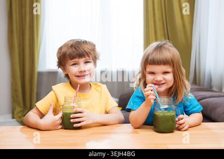 Two Cute smiling kids drinks healthy green smoothie with straw in a jar mug on a gray background Stock Photo