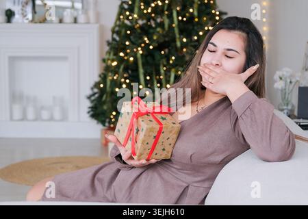 Young woman in gray dress carrying christmas gifts yawning Stock Photo