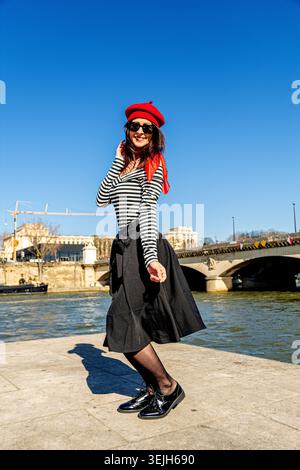 Young woman jumping with joy in french style on seine riverbank in paris Stock Photo