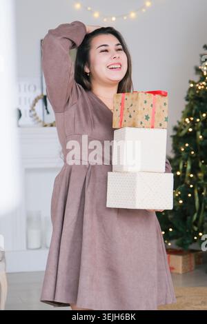 Packaging holiday gifts. Christmas gift wrapping. Young woman in gray dress carrying christmas gifts Stock Photo