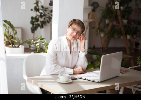 Attractive aged businesswoman is using a smartphone sitting at a table Stock Photo