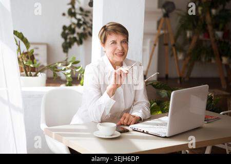 Attractive aged businesswoman is using a smartphone sitting at a table Stock Photo