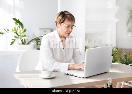 Attractive aged businesswoman is using a smartphone sitting at a table Stock Photo