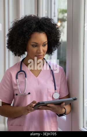 African American female nurse wearing stethoscope and using tablet touchscreen in hospital corridor. Healthcare, professionalism, technology, medical, Stock Photo
