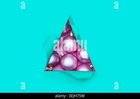 Xmas baubles pink color in triangular Torn hole and ripped of paper in a shape of Christmas tree. Christmas flat lay Stock Photo