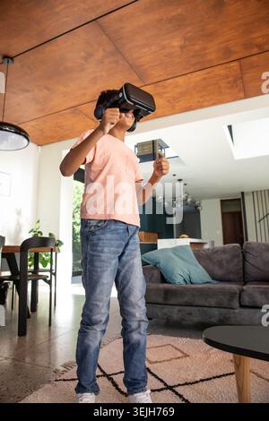African American child using virtual reality headset and headphones on rug in living room. Technology, leisure, innovation, modernity, entertainment, Stock Photo