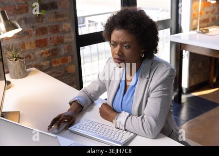 African American woman working at desk in office, typing on white keyboard under metal desk lamp. Professional, workspace, modern, interior, productiv Stock Photo