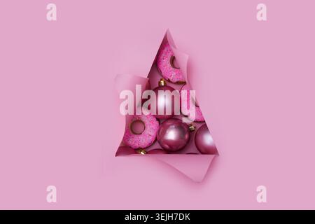 Xmas baubles pink color in triangular Torn hole and ripped of paper in a shape of Christmas tree. Christmas flat lay Stock Photo