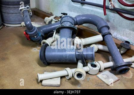 A disassembled pile of grey and white PVC industrial plumbing pipes and fittings on a workshop floor. Stock Photo