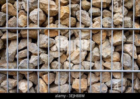 Modern gabion wall made of natural brown stones enclosed in a durable gray metal wire mesh cage. Stock Photo
