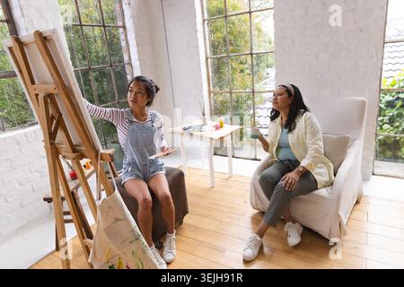 Diverse female artists painting on easel in art studio, instructor holding ceramic mug, copy space. Creativity, collaboration, i Stock Photo