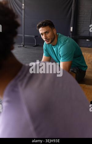 Male workout partners leaning forward listening to training tips on wooden plyometric box at gym. Fitness, strength, training, gym, determination, cam Stock Photo