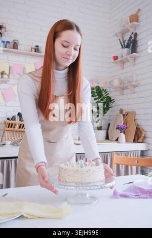 Caucasian woman serving table for Easter dinner, putting plates, cutlery and sweet cake Stock Photo