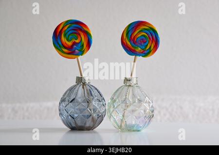 Two vibrant swirl lollipops standing inside small decorative glass bottles on a bright background. Stock Photo