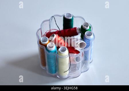 A plastic organizer box filled with various colorful sewing thread spools on a white surface. Stock Photo