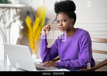 Portrait of African-American millennial student woman with afro hairstyle looking at camera while making researches browsing inf Stock Photo