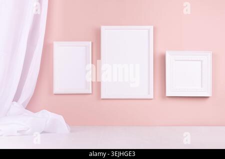 Calm pastel pink interior with set of white blank photo frames for text, design, poster, pictures hanging on pastel pink wall wi Stock Photo