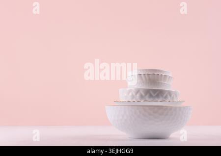 White ceramic dishes with thin gold border, different tracery form on white wood table in delicate pastel pink interior. Stock Photo