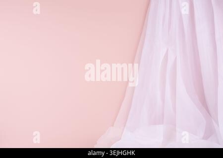 Soft light scene with airy folded white silk curtain on pastel pink wall. Abstract background. Stock Photo