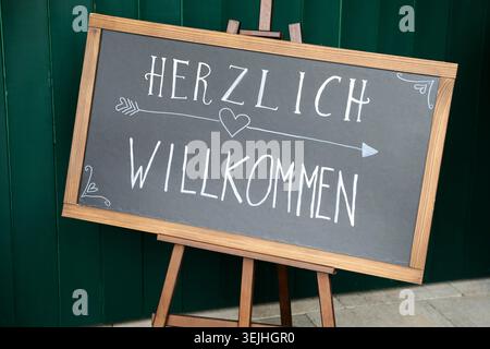 A chalkboard sign with the handwritten German text "Herzlich Willkommen" on a wooden easel. Stock Photo