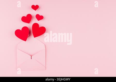 Opened paper envelope with fly out red hearts on soft pink color background. Copy space. Valentine day concept for design. Stock Photo