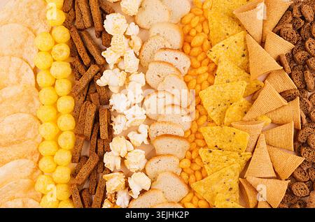Assortment crunchy snacks - popcorn, nachos, croutons, corn sticks, potato chips as decorative background, top view, closeup. Stock Photo