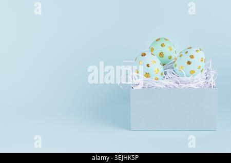 Simple and minimal easter background - easter eggs with golden dots in gift box on blue backdrop. Stock Photo