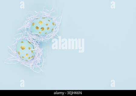 Easter background - easter eggs with golden dots in white nest on blue backdrop, top view. Stock Photo