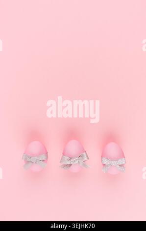 Elegant easter eggs with silver bows in row on pastel pink background, vertical, stories. Stock Photo
