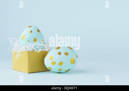 Elegant easter eggs with gold dots and golden gift box on blue background, copy space. Stock Photo