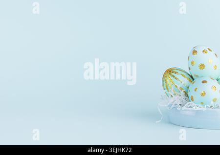 Handmade blue easter eggs with golden glitter design on bowl on blue background, closeup. Stock Photo