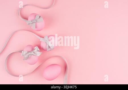 Festive easter background - pink easter eggs with silver bow and curled ribbons as border on pastel pink backdrop. Stock Photo
