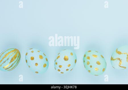Elegant easter eggs with gold design as border on blue background, copy space, top view. Stock Photo