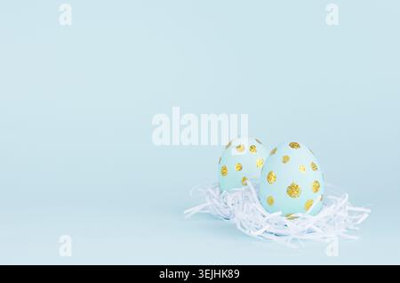 Blue easter eggs with gold glitter dots in white nest on blue background, copy space. Stock Photo