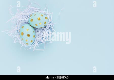 Stylish easter background - blue easter eggs with gold dots in white nest on blue color, top view. Stock Photo