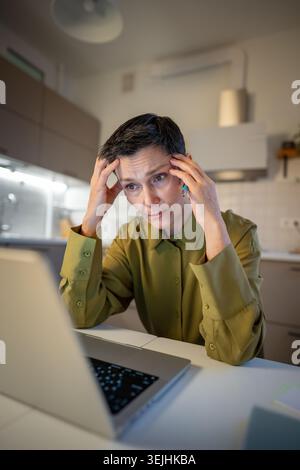 Tired senior businesswoman sitting at table looking at laptop screen with empty expression, feeling exhausted having headache du Stock Photo